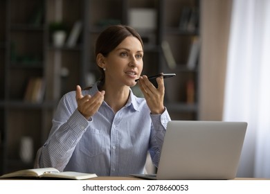 Attractive young woman sit at desk holding smart phone talk on speaker phone, share information, provide professional support to client using modern wireless tech and connection. Voicemails concept