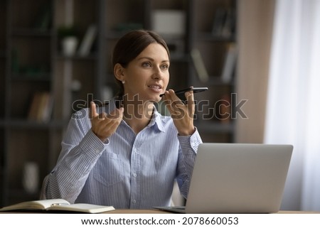Attractive young woman sit at desk holding smart phone talk on speaker phone, share information, provide professional support to client using modern wireless tech and connection. Voicemails concept