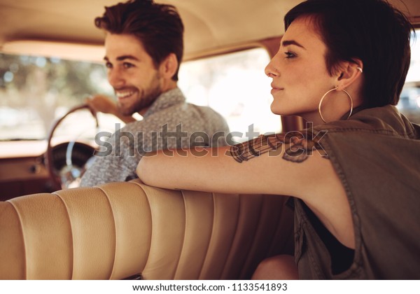 Attractive young\
woman sitting in the backseat of a car with man driving. Friends\
traveling by a car. Road\
trip.