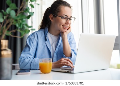 Attractive young woman sitting at the kitchen table, working on laptop computer - Powered by Shutterstock