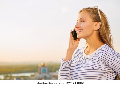 Attractive young woman smiling looking away talking on the phone observing the city from a rooftop