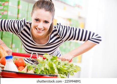 Attractive young woman smiling and pushing a cart at supermarket.