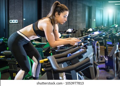 Attractive Young Woman In Sportswear Cycling In Gym.