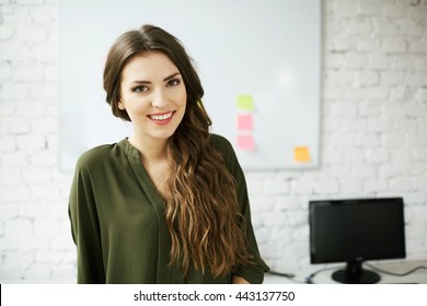 Attractive young woman standing in office against white brick wall