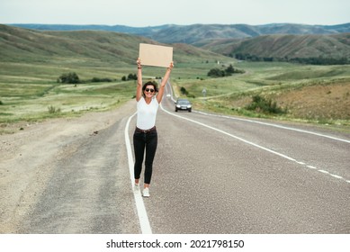 Attractive young woman standing on a highway and catching a passing car. The concept of hitchhiking tourism. A traveling woman is hitchhiking on the road. A woman is hitchhiking on the road. Vacation