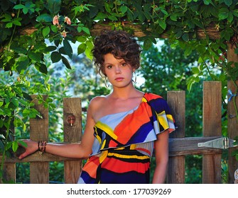 Attractive young woman with a sultry look, wearing an off the shoulder dress in a garden.
