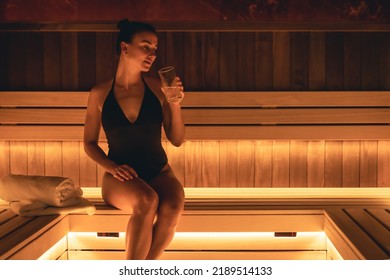 Attractive young woman in a swimsuit with a glass of water in the sauna.