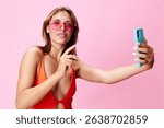 Attractive young woman in swimsuit taking a selfie with smartphone in hand on vibrant pink background