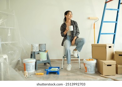 Attractive young woman taking a break during a home renovation project, sitting on the floor surrounded by painting supplies. - Powered by Shutterstock