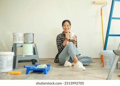 Attractive young woman taking a break during a home renovation project, sitting on the floor surrounded by painting supplies. - Powered by Shutterstock