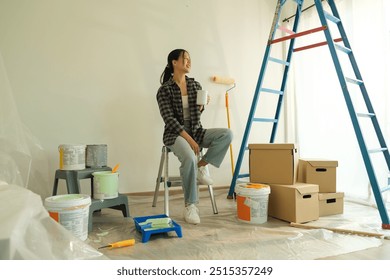 Attractive young woman taking a break during a home renovation project, sitting on the floor surrounded by painting supplies. - Powered by Shutterstock