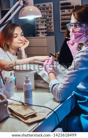 Attractive young woman with tattoo is getting nail care from expirienced manicurist.