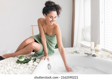 Attractive Young Woman In Towel Preparing Hot Foamy Bath, Touching Water, Checking Temperature, Enjoying Home Spa Procedure, Blank Space. Wellness, Body Care, Hygiene Concept