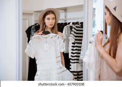Attractive young woman trying on dress in front of mirror in clothing store
