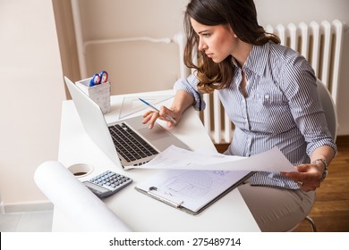 Attractive young woman using laptop and working on her finances at home 