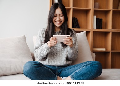 Attractive Young Woman Using Mobile Phone While Relaxing On A Couch At Home