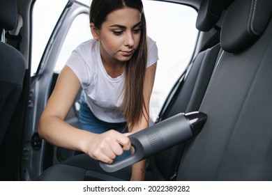 Attractive young woman using portable vacuum cleaner in her car  Woman vacuuming her car in the garage at home  Car interior cleaning