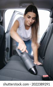Attractive young woman using portable vacuum cleaner in her car. Woman vacuuming her car in the garage at home. Car interior cleaning