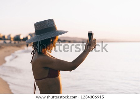 Attractive young woman using a smart phone at the beach while sunlight is a beautiful/ young hipster girl on a holidays holding a gadget 