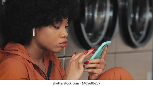 Attractive young woman using smartphone at laundromat. She is wearing a wireless earphones and singing indoors. - Powered by Shutterstock