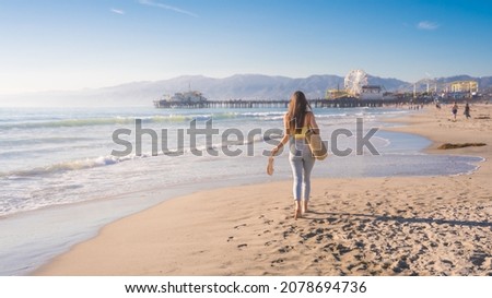 Attractive young woman walking towards Santa Monica beach pier, Los Angeles, California