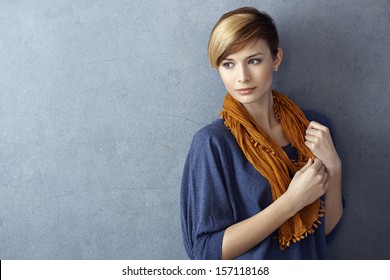 Attractive young woman wearing scarf standing by grey wall, looking away. Copy space.