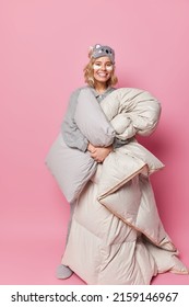 Attractive Young Woman Wears Blindfold Holds Comfy Blanket And Pillow Applies Beauty Pads To Remove Wrinkles Going To Have Rest After Hard Day Isolated Over Pink Background. Waking Up Concept