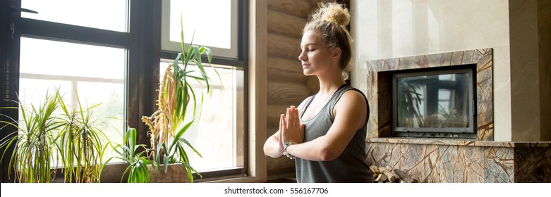Attractive young woman working out at home, doing yoga exercise on blue mat, sitting in Easy Posture with Namaste, meditating, breathing, relaxing. Horizontal photo banner for website header design