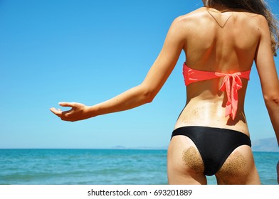 Attractive young woman's back and butt in bikini on the beach looking at the sea