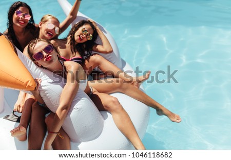 Attractive young women floating together on a big inflatable swan in pool. Woman making a pout with her friends relaxing in an inflatable toy in pool.