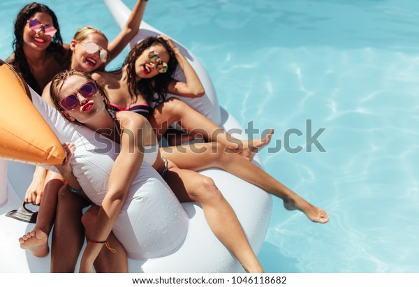 Attractive young women floating together on a\
big inflatable swan in pool. Woman making a pout with her friends\
relaxing in an inflatable toy in\
pool.