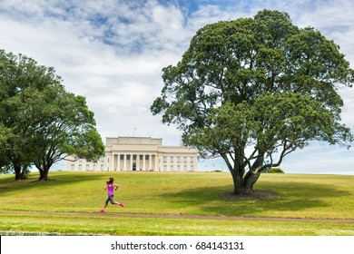 Auckland City Park Running Jogging Girl On Green Grass And Trees At Auckland Domain Park With Memorial Museum . Active Lifestyle Woman Training. Famous Travel Tourist Attraction In New Zealand.