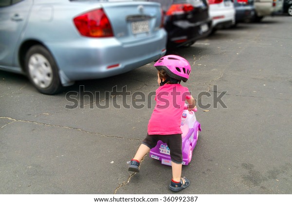 AUCKLAND - JAN 11 2016:Small girl (Naomi\
Ben-Ari age 1-2) rid a toy car in parking lot. The U.S. Center for\
Disease Control reported that about 300 fatalities per year result\
from backup\
collisions.