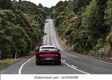 Auckland  New Zealand - January 10 2020: View of Mazda 3 driving on straight hilly road through Waitakere Ranges forest towards Piha village, away from camera