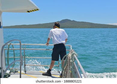 Auckland, New Zealand - January 5, 2021: View of crew member (deckhand) on board Fullers ferry with Rangitoto Island in background