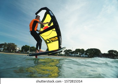 Auckland, New Zealand - October 9, 2019: A man wingfoils off Kohimarama Beach in Auckland, riding a stand up paddleboard with a hydrofoil.