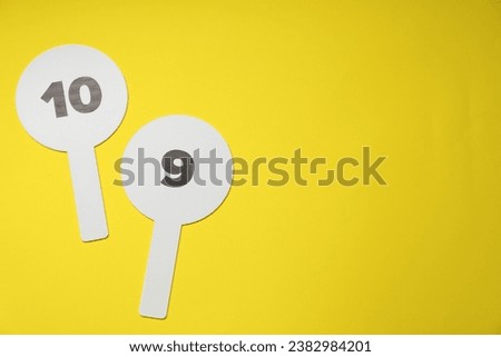 Auction paddles with numbers on yellow background, flat lay. Space for text