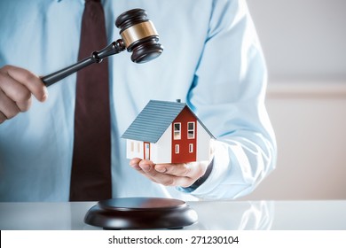 Auctioneer Knocking Down A Property Sale Holding A Model House As He Raises His Gavel, Or A Lawyer Or Judge Mediating In A Property Dispute In Court