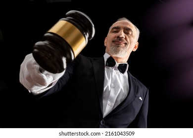 Auctioneer, salesperson with gavel at public auction. Senior male barker in formal elegant suit with auction hammer for close the bidding.