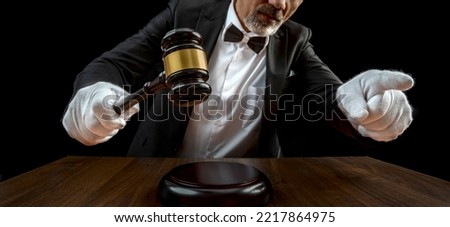 Auctioneer, salesperson with gavel at public auction. Senior male barker in formal elegant suit with auction hammer for close the bidding.