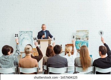 auctioneer talking with microphone and looking at buyers with auction paddles during auction - Shutterstock ID 1657604125