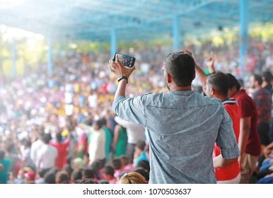 Audience are dancing has fun with taking photo at a music festival on stadium. Rear view.