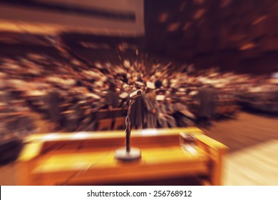Audience in hall during graduation ceremony. Microphone and stand in front. Concept of graduation, audience or stage fright. Radial zoom effect defocusing filter applied, with vintage instagram look.