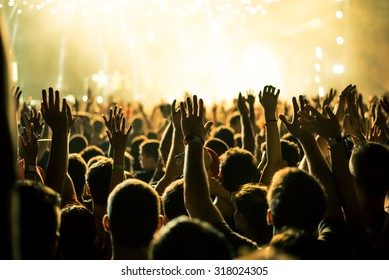 Audience with hands raised at a music festival and lights streaming down from above the stage. Soft focus, blurred movement. - Shutterstock ID 318024305