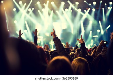 Audience With Hands Raised At A Music Festival And Lights Streaming Down From Above The Stage