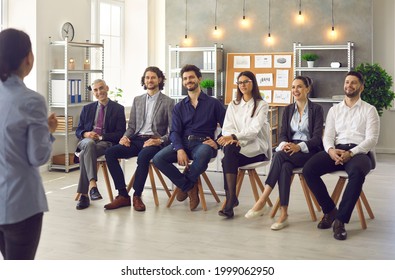 Audience Listening To Speaker. Small Group Of Happy People Sitting In Row Listening To Corporate Psychologist, Business Trainer Or Life Coach During Master Class Meeting In Modern Office Interior