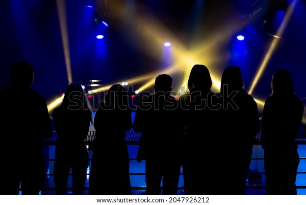 The\
audience looks at the variety show, the rays of stage lights.\
Silhouettes of people in the beams of\
searchlights.
