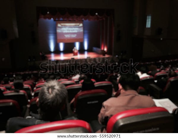 Audience meeting community in\
seminar hall with ted talk live show blur image use for background.\
Ted talk show with many crowd on play stage of theatre\
concept.