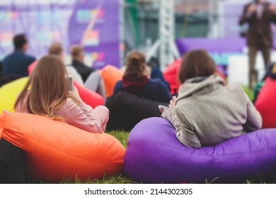 Audience At The Open Air Venue Listens To Lecturer, People On A Bean Bags Together Listen To Speaker On Stage At Master-class, Corporate Business Seminar Outdoors
