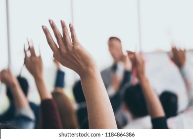 Audience raising hands up while businessman is speaking in training at the office.